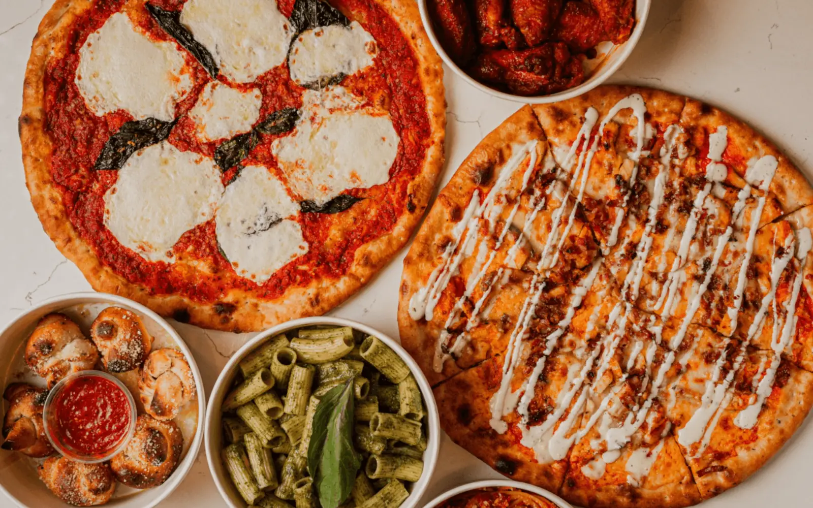 Margherita and buffalo chicken thin-crust pizzas with wings and pasta